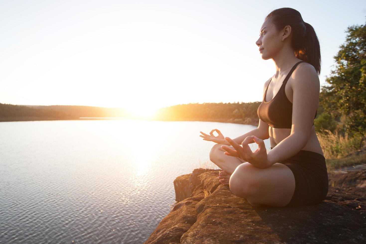 Junge gesunde Frau praktiziert Yoga am Bergsee während des Sonnenuntergangs. foto