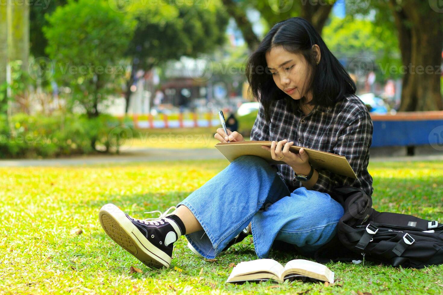 schön asiatisch jung Frau Hochschule Schüler konzentriert Schreiben auf Notizbuch und lesen Buch im draußen Stadt Park foto