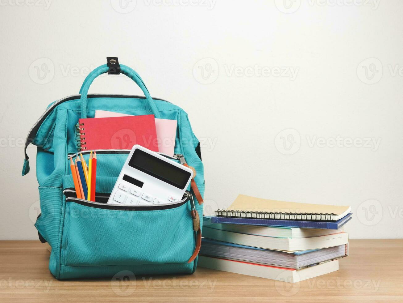 Vorderseite Aussicht von Grün Rucksack mit Schule liefern, Stapel von Bücher auf hölzern Tabelle und Weiß Hintergrund mit Kopieren Raum. foto