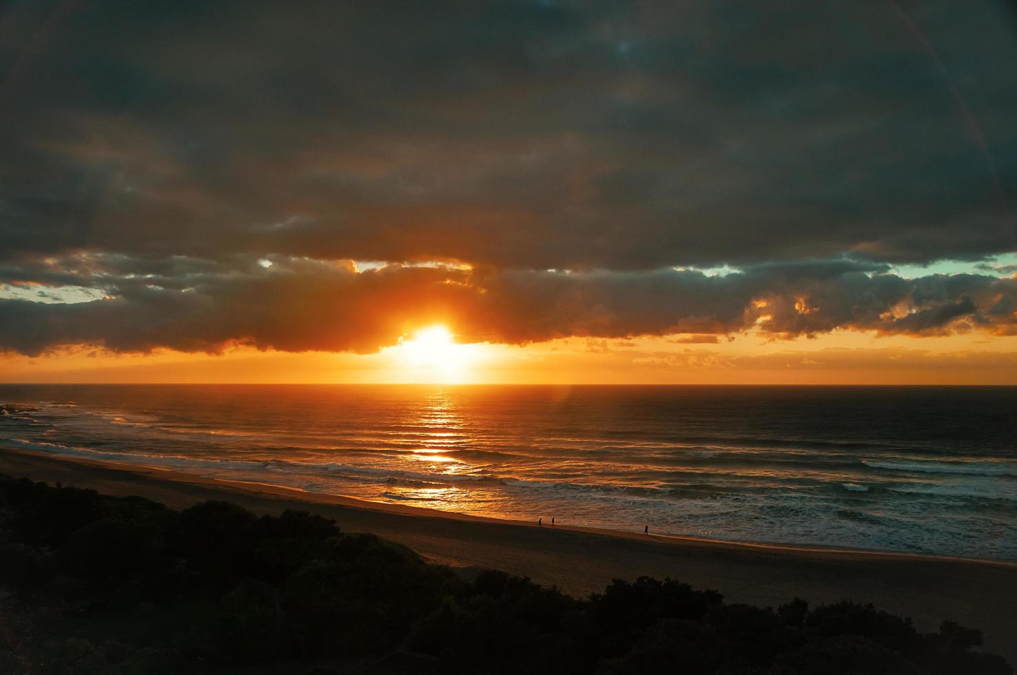 Früher Sonnenaufgang am Ozeanstrand, Menschensilhouetten, dramatische Wolken foto