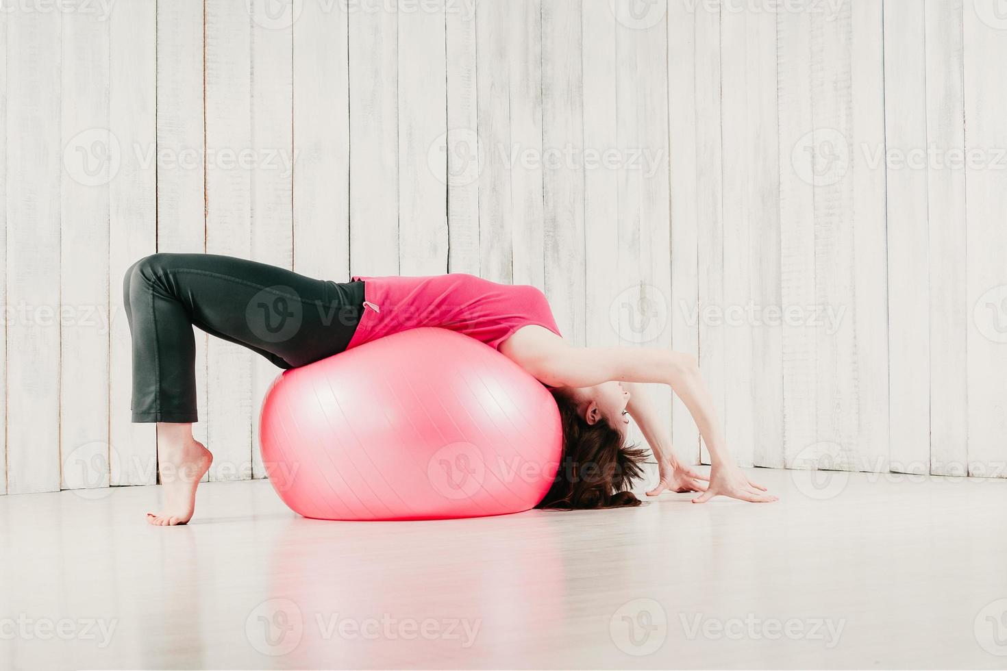 ein Mädchen in einem rosa Top, das in einem Fitnessstudio eine Brücke auf einem rosa Fitball schlägt foto