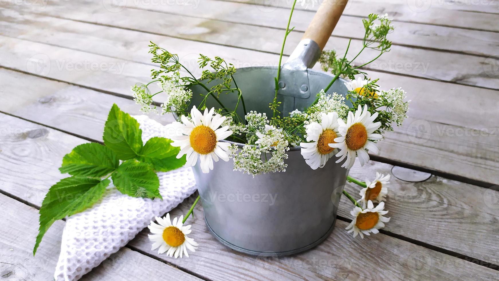 Metalleimer mit einem Strauß Gänseblümchen und einem weißen Handtuch. foto