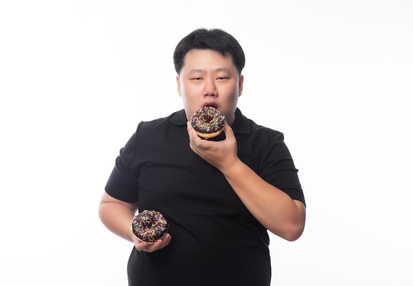 junger lustiger fetter asiatischer Mann, der Schokoladenkrapfen isst foto