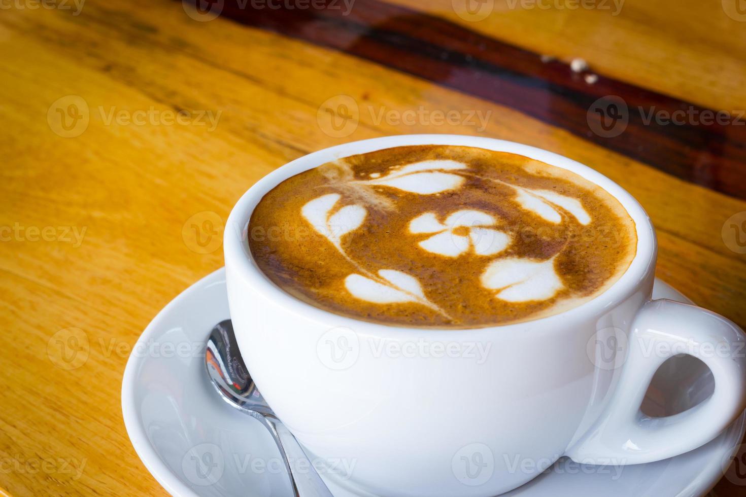 Heißer Kaffee mit Blume aus Milchschaum auf Holztisch. foto