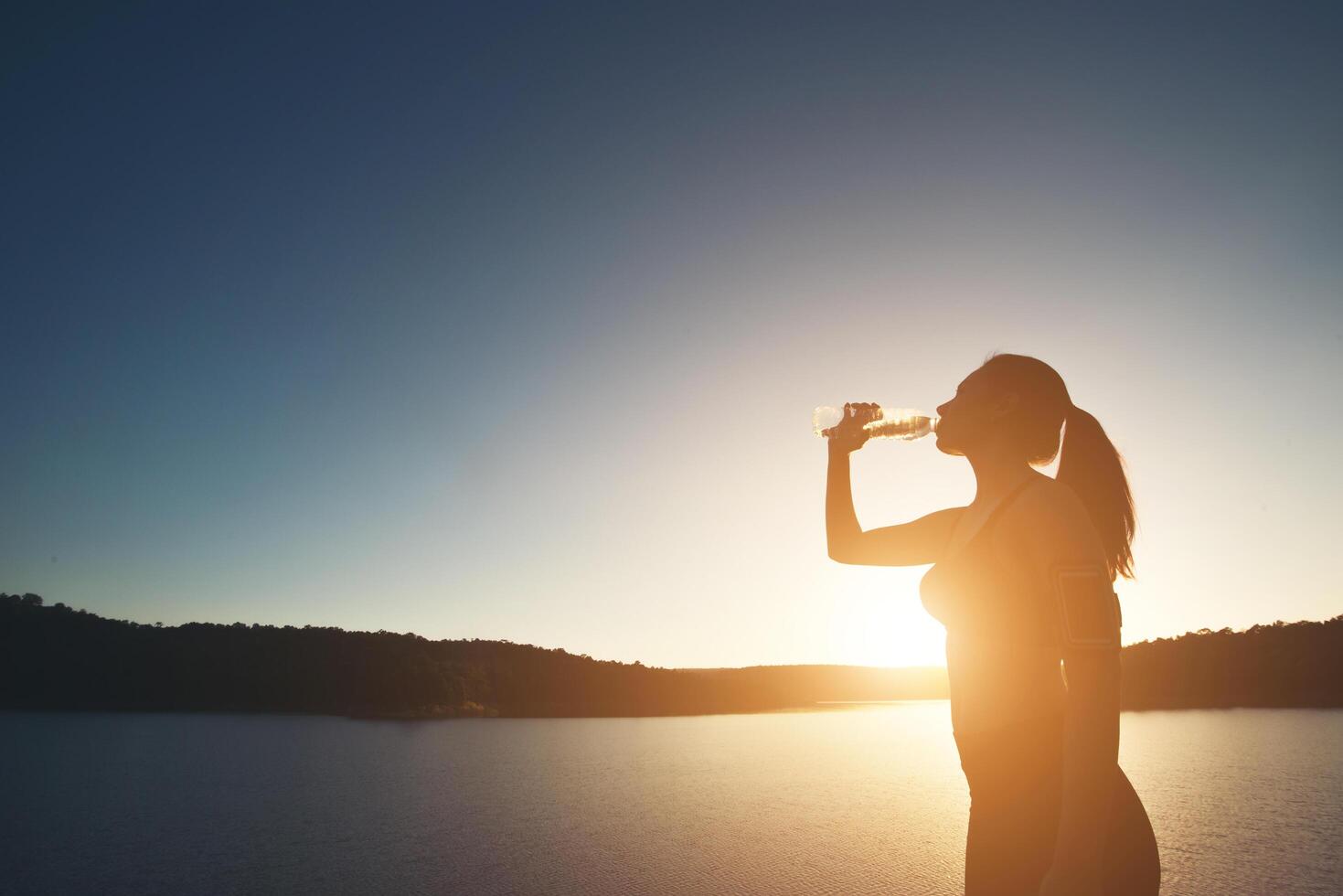 Frau wandert auf den Gipfel des Berges und trinkt Wasser bei Sonnenuntergang foto