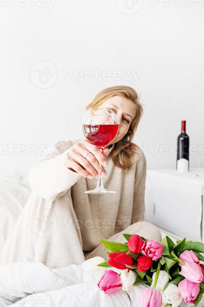 Frau sitzt auf dem Bett und hält ein Glas Wein foto