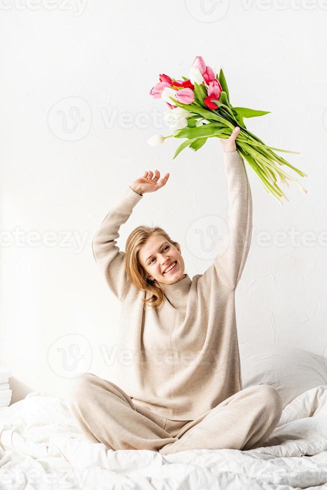 Frau tanzt auf dem Bett mit Tulpenstrauß foto