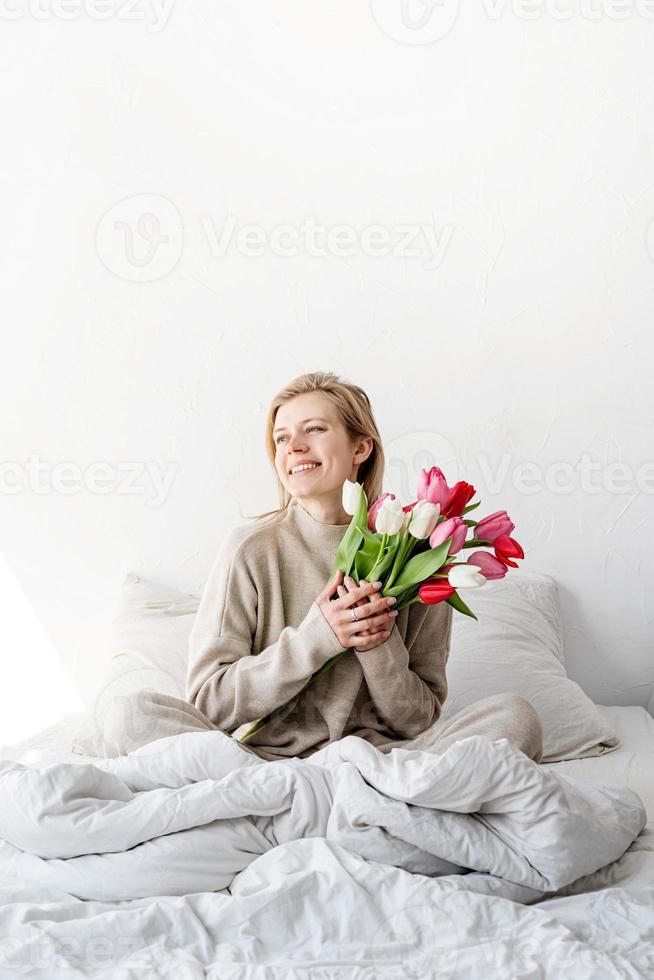 Frau sitzt auf dem Bett und hält Tulpenblumen foto
