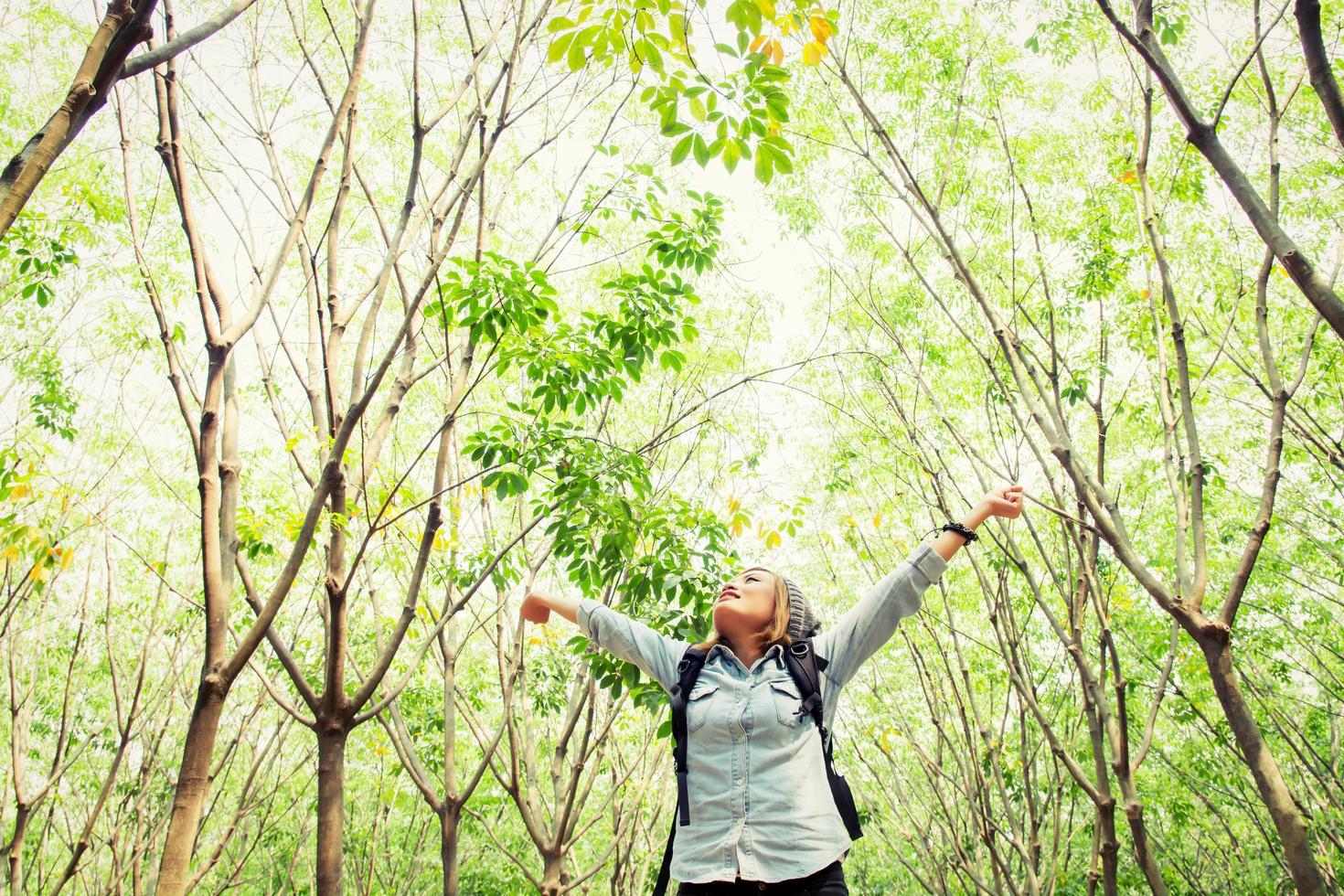 Frauenrucksack, der im Wald spazieren geht, die Hände glücklich mit frischer Luft ausstrecken foto