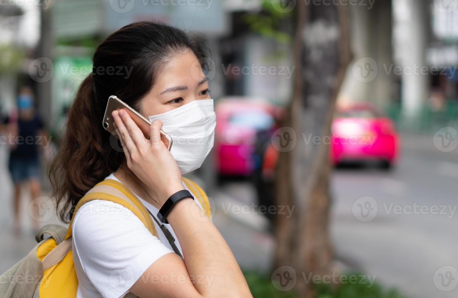 junge Frau, die während des Ausbruchs von Covid 19 eine Maske mit Smartphone trägt. foto