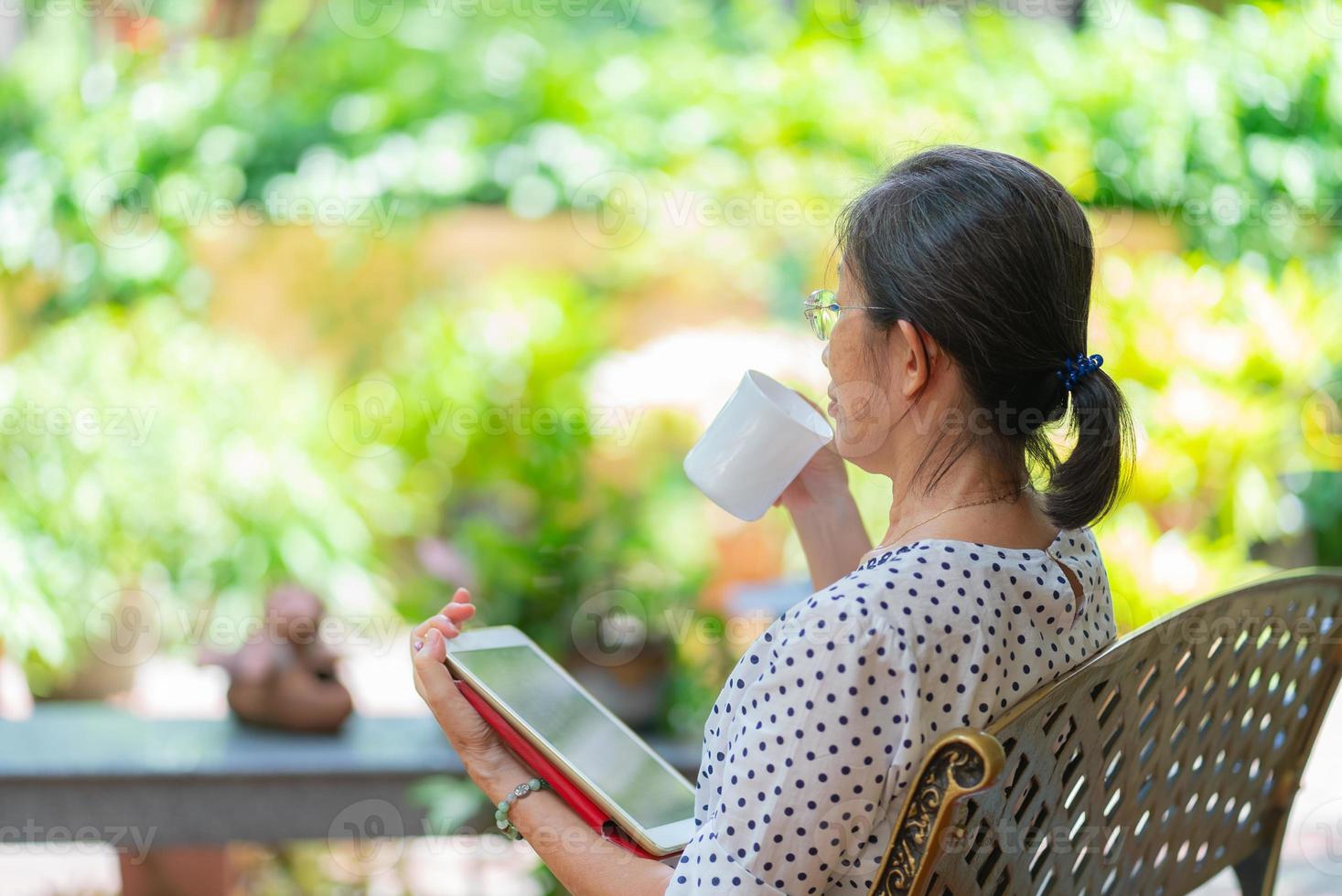 Ältere asiatische Frau, die Kaffee trinkt, während sie Tablet verwendet, um E-Mails zu lesen? foto