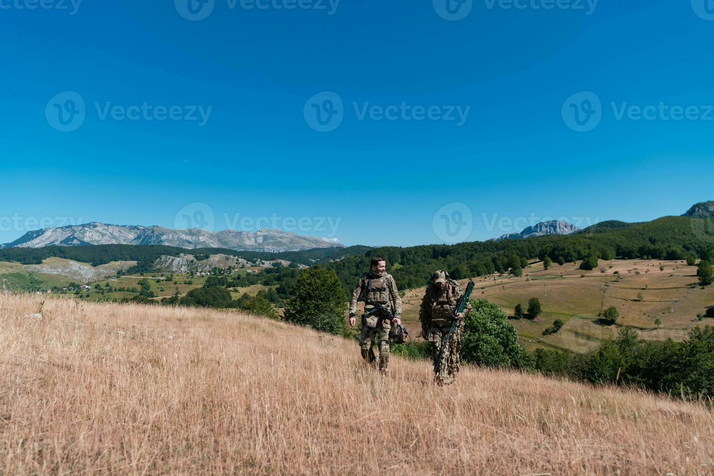 ein Scharfschütze Mannschaft Kader von Soldaten ist gehen verdeckt. Scharfschütze Assistent und Mannschaft Führer Gehen und Zielen im Natur mit Gelb Gras und Blau Himmel. taktisch tarnen Uniform. foto