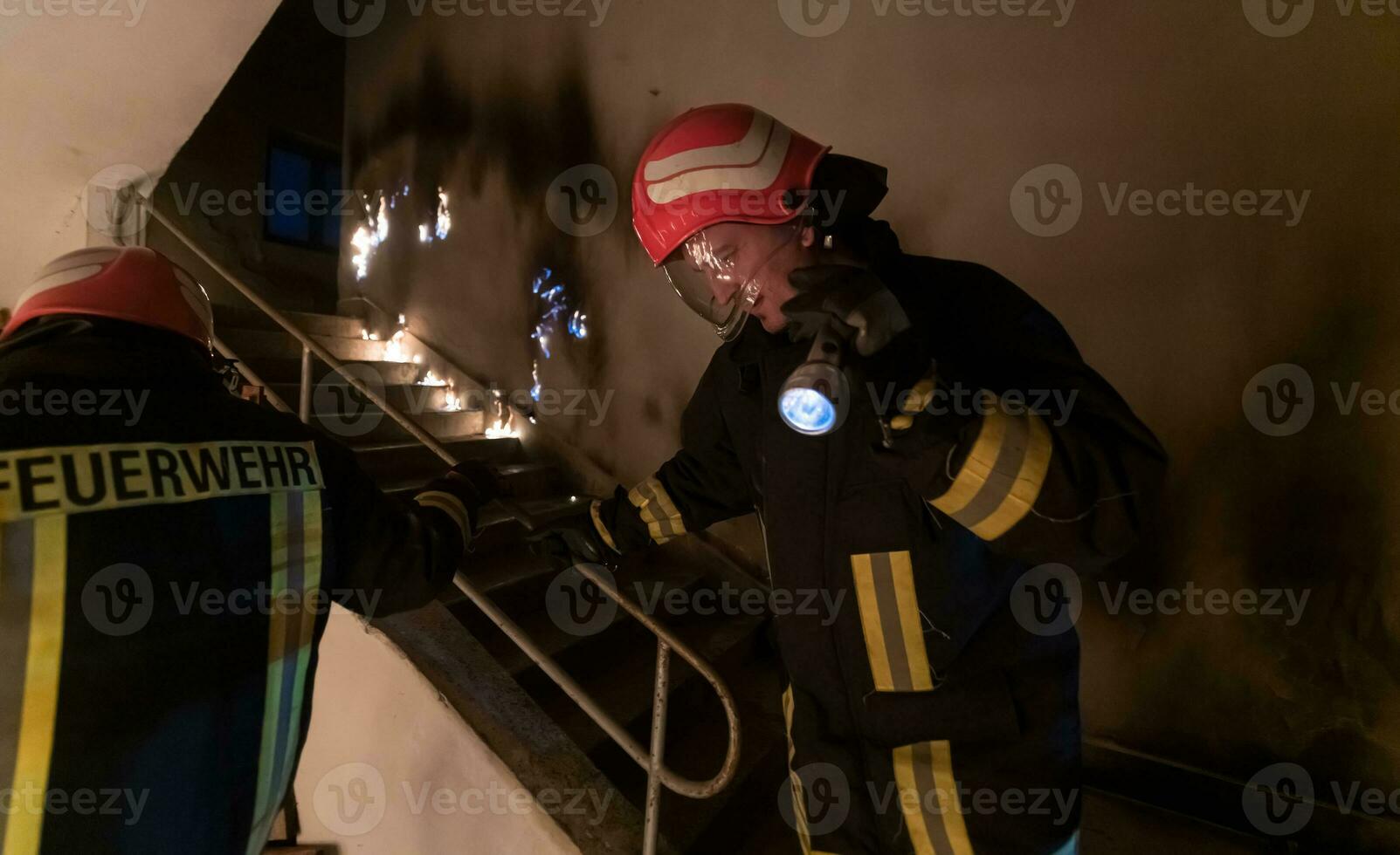 mutig Feuerwehrmann sinkt ab Treppe von ein Verbrennung Gebäude und hält Gerettet Mädchen im seine Waffen. öffnen Feuer und einer Feuerwehrmann im das Hintergrund. foto