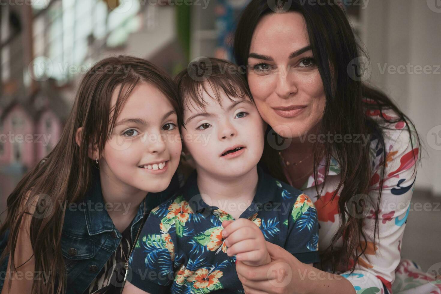 ein Mädchen und ein Frau Umarmung ein Kind mit Nieder Syndrom im ein modern Vorschule Institution foto