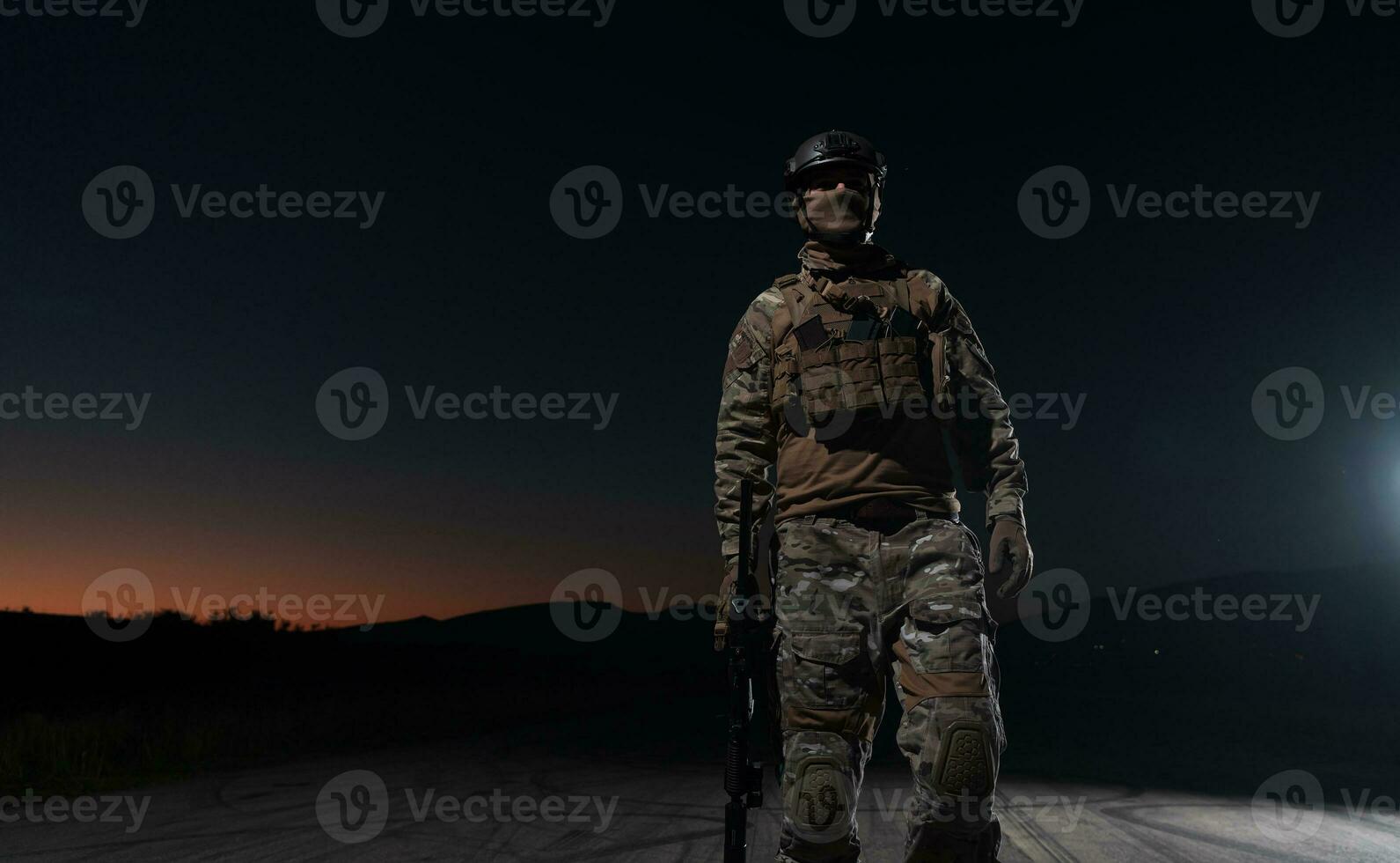 Heer Soldat im Kampf Uniformen mit ein Angriff Gewehr, Teller Träger und Kampf Helm gehen auf ein gefährlich Mission auf ein regnerisch Nacht. foto