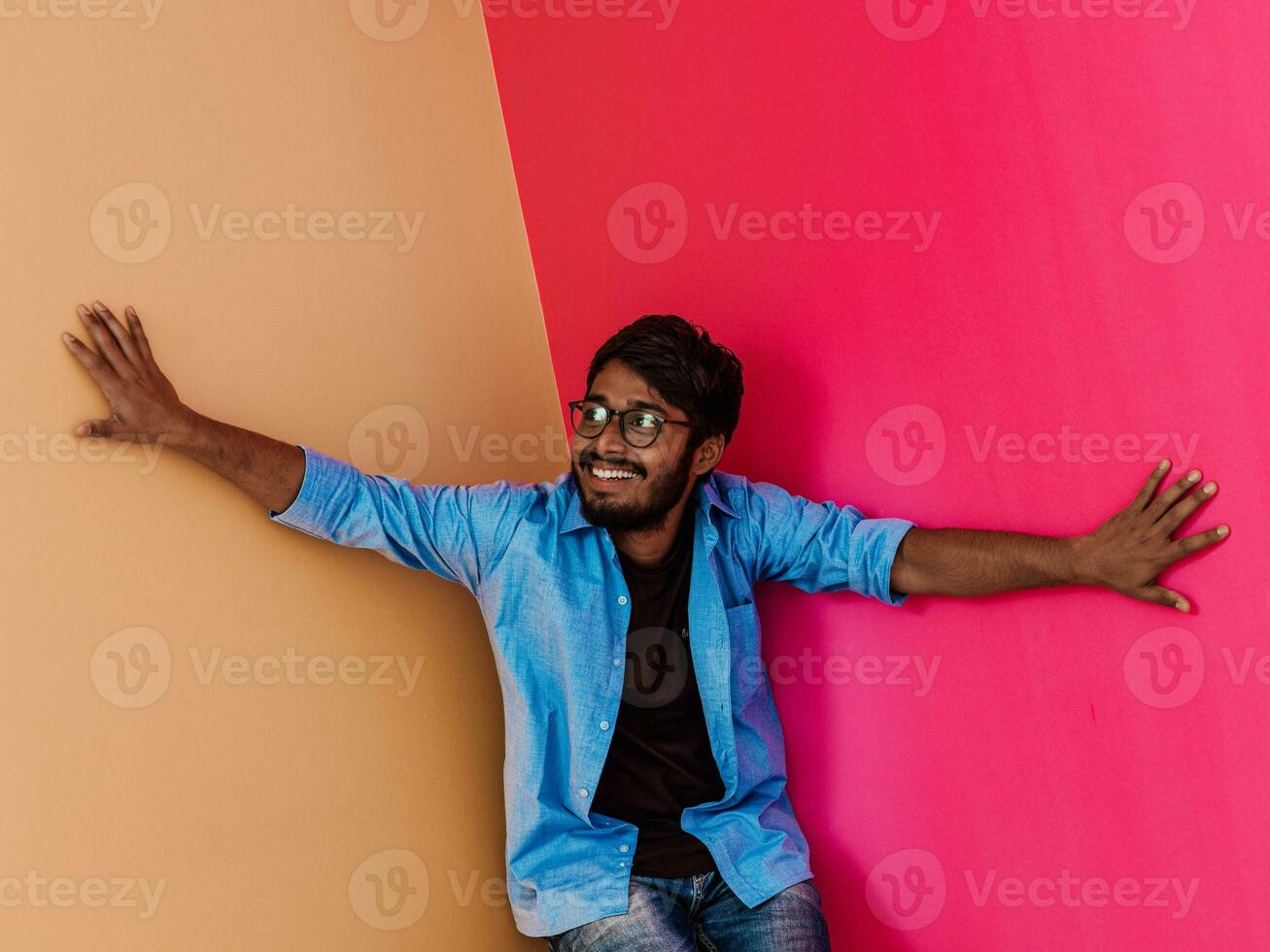 ein jung indisch Schüler im ein Blau Hemd mit Brille posieren auf rosa-orange Hintergrund foto