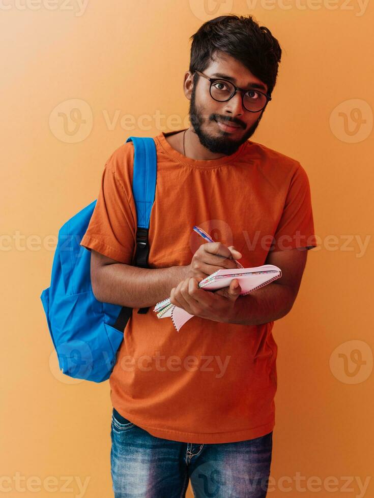 indisch Schüler mit Blau Rucksack, Brille und Notizbuch posieren auf Orange Hintergrund. das Konzept von Bildung und Schulung. Zeit zu gehen zurück zu Schule foto