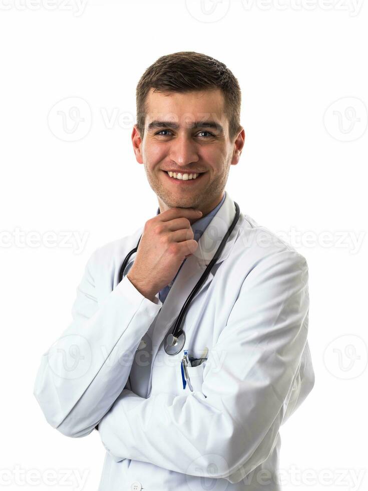Porträt von Held im Weiß Mantel. heiter lächelnd jung Arzt mit Stethoskop im medizinisch Krankenhaus Stehen gegen Weiß Hintergrund. Coronavirus covid-19 Achtung warnen foto