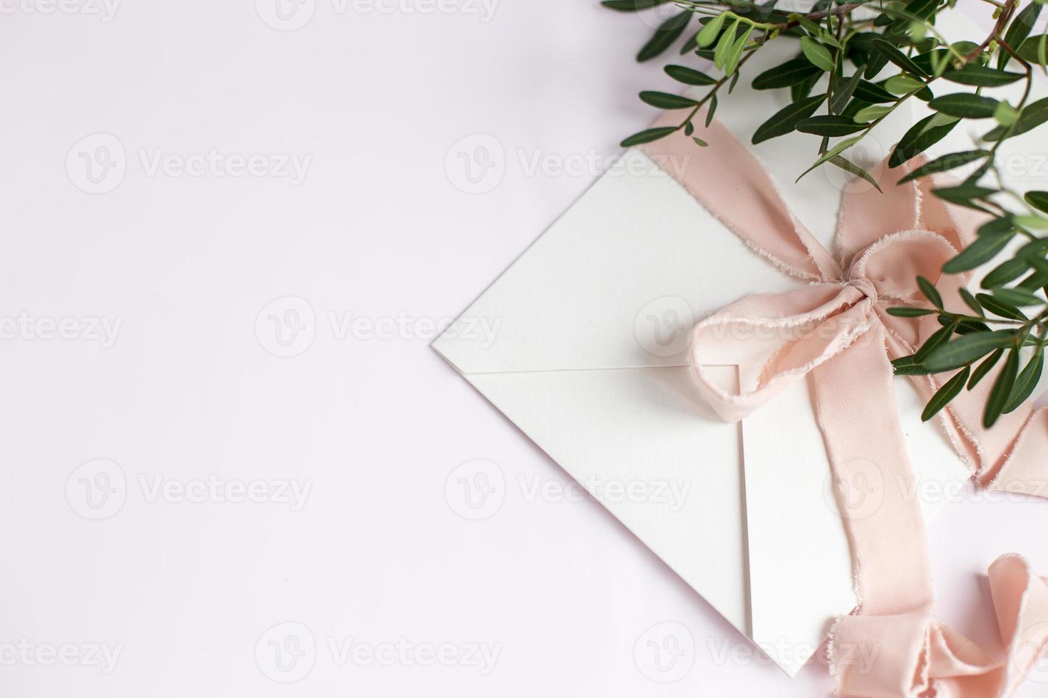 Umschlag auf weiß-rosafarbenem Hintergrund mit pfirsichfarbenem Seidenband und rosa foto