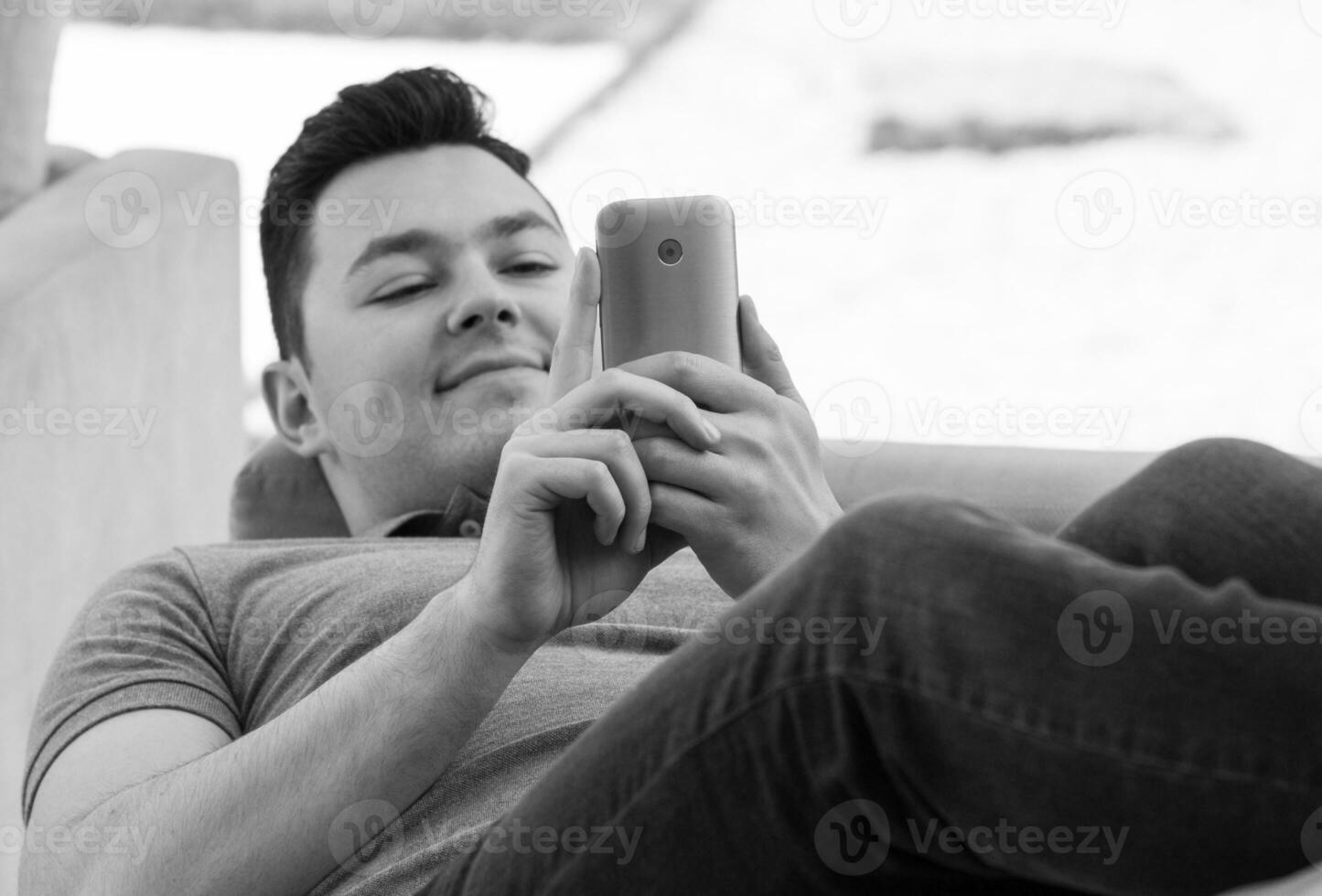 jung Mann mit Handy, Mobiltelefon während Lügen auf Couch foto