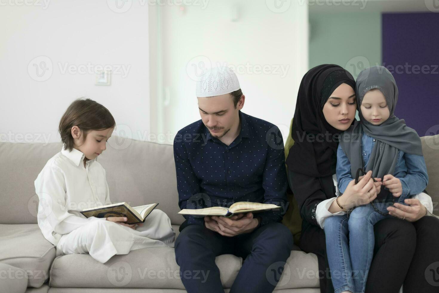 traditionell Muslim Familie Eltern mit Kinder lesen Koran und beten zusammen auf das Sofa Vor iftar Abendessen während ein Ramadan Fest beim Zuhause foto