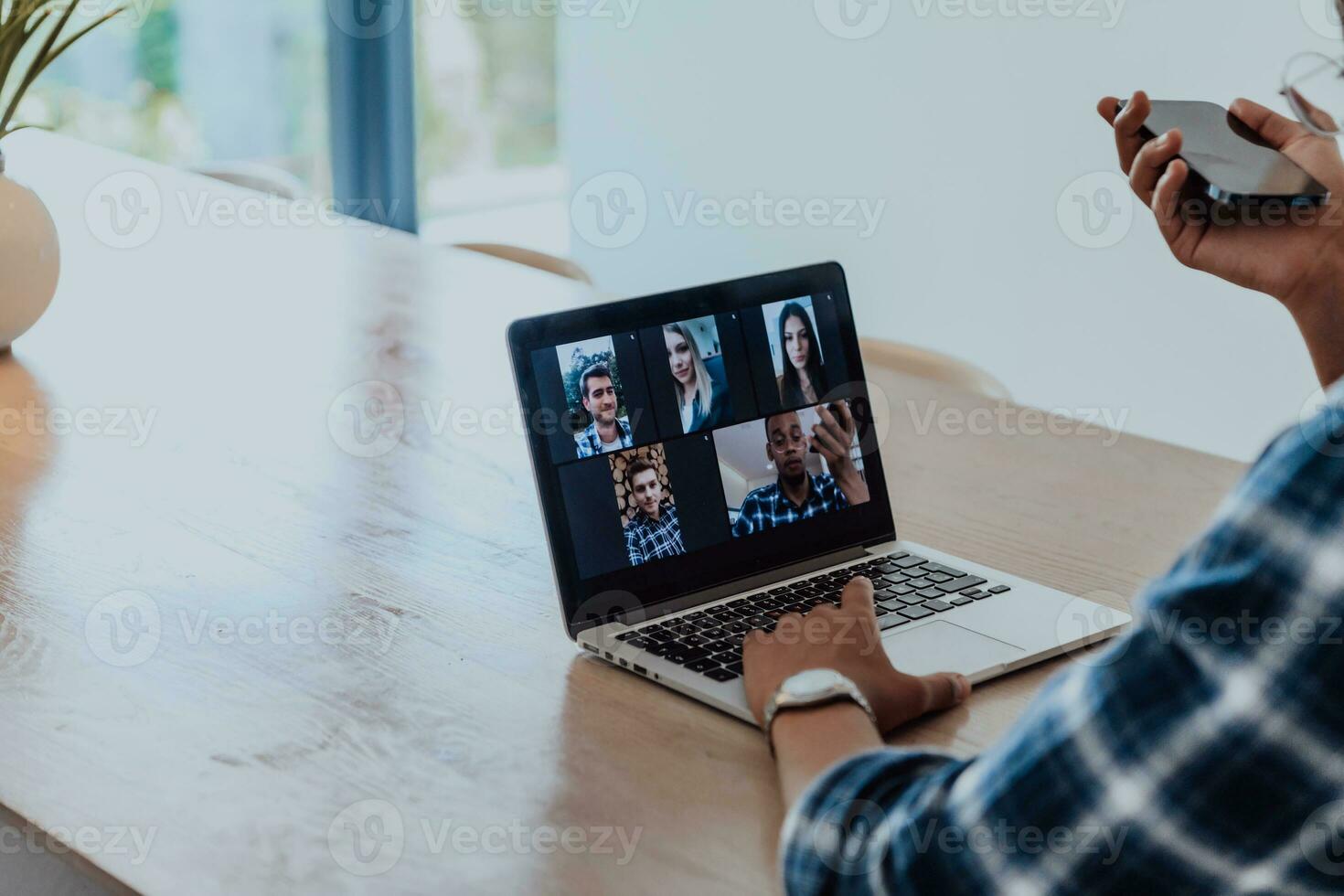 afrikanisch amerikanisch Mann im Brille Sitzung beim ein Tabelle im ein modern Leben Zimmer, mit ein Laptop und Smartphone zum Geschäft Video Plaudern, Konversation mit freunde und Unterhaltung foto