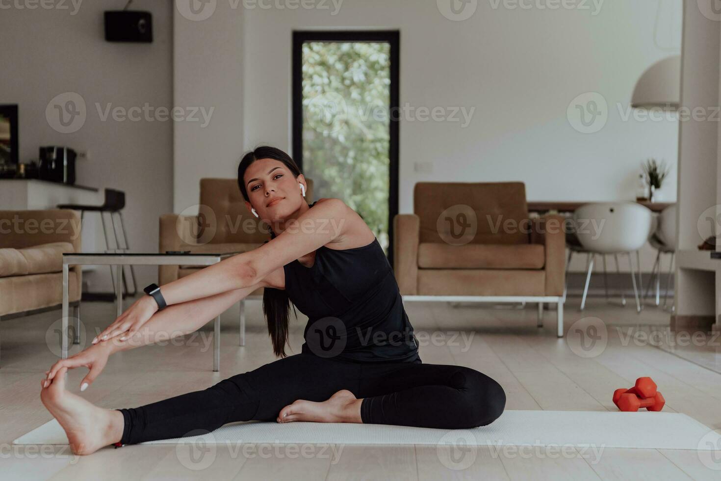 ein jung Frau im Sportbekleidung Dehnen ihr Beine während online Ausbildung während das Pandemie während Ausbildung im das Leben Zimmer von ihr Zuhause foto