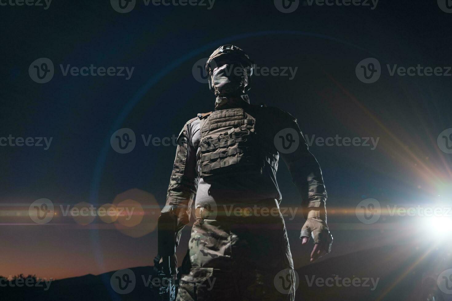 Heer Soldat im Kampf Uniformen mit ein Angriff Gewehr, Teller Träger und Kampf Helm gehen auf ein gefährlich Mission auf ein regnerisch Nacht. foto