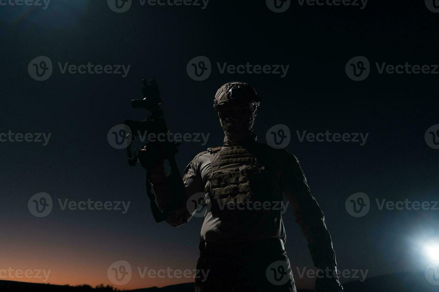 Heer Soldat im Kampf Uniformen mit ein Angriff Gewehr, Teller Träger und Kampf Helm gehen auf ein gefährlich Mission auf ein regnerisch Nacht. foto