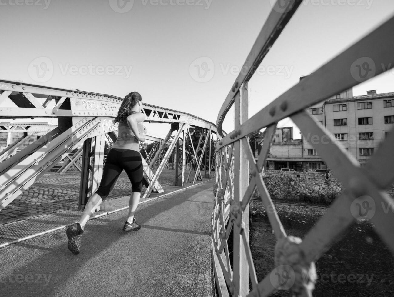 Frau, die am sonnigen Morgen über die Brücke joggt foto