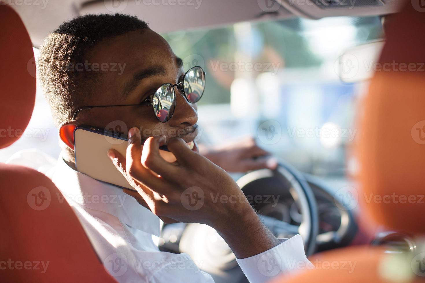 glücklicher Afroamerikaner, der im Sommer ein Auto mit einem Telefon fährt foto