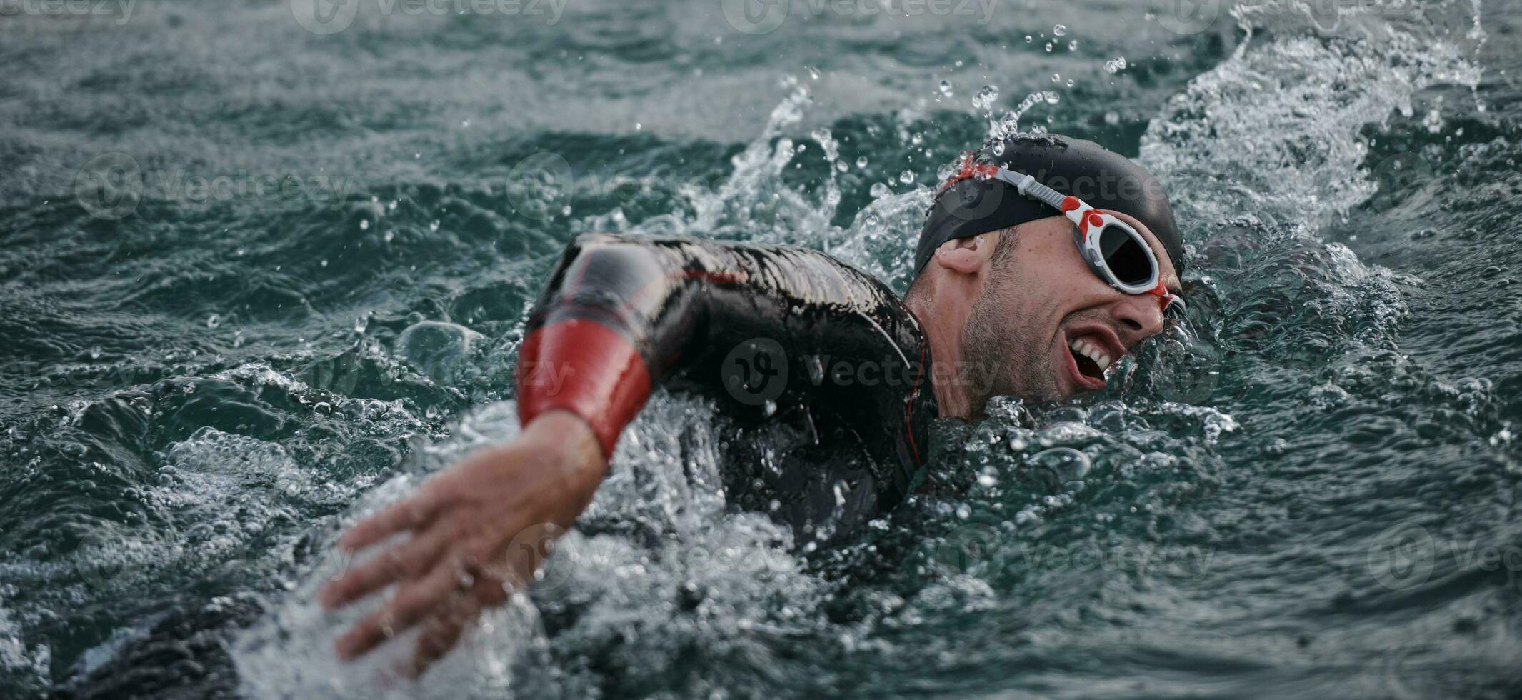 Triathlon-Athlet, der bei Sonnenaufgang auf dem See schwimmt und einen Neoprenanzug trägt foto