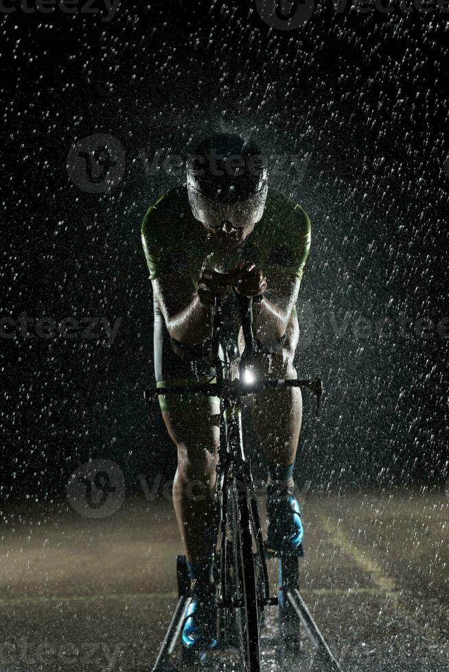 Triathlon-Athlet, der in regnerischer Nacht schnell Fahrrad fährt foto