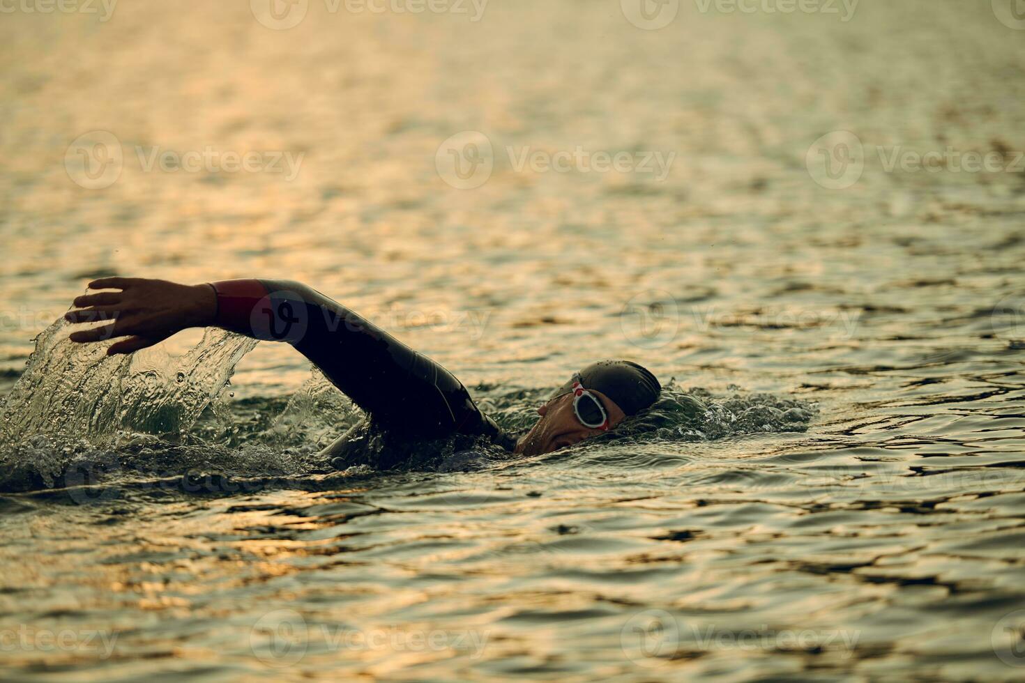 Triathlon-Athlet, der bei Sonnenaufgang auf dem See schwimmt und einen Neoprenanzug trägt foto