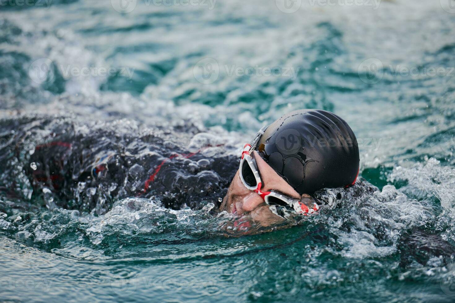 Triathlon-Athlet, der bei Sonnenaufgang auf dem See schwimmt und einen Neoprenanzug trägt foto