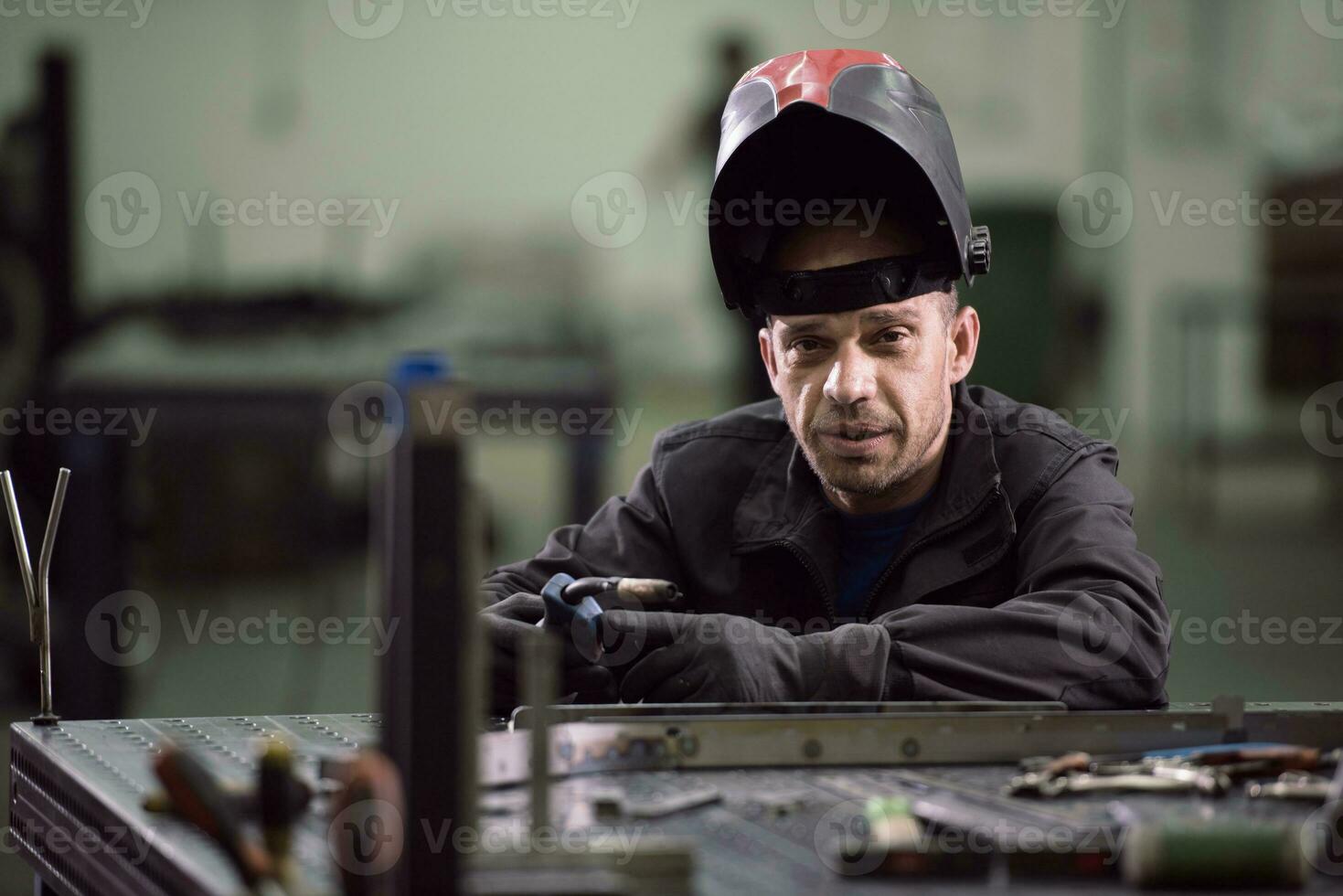 Porträt eines jungen professionellen Ingenieurs der Schwerindustrie. Arbeiter mit Sicherheitsweste und Helm, der vor der Kamera lächelt. im Hintergrund unfokussierte große Industriefabrik foto