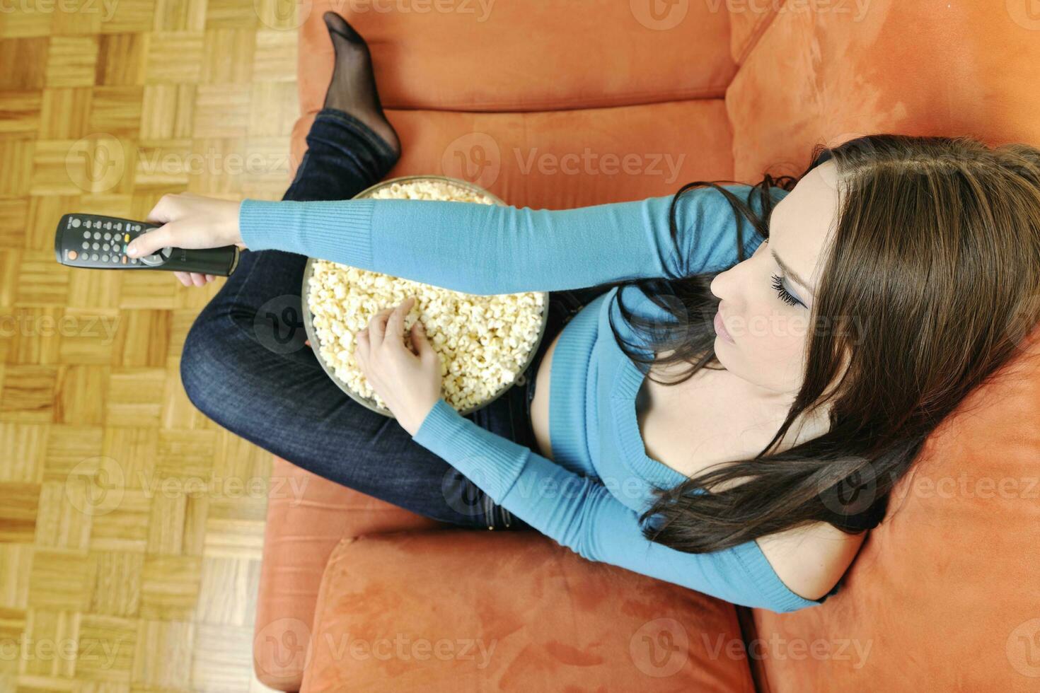 Junge Frau isst Popcorn auf orangefarbenem Sofa foto