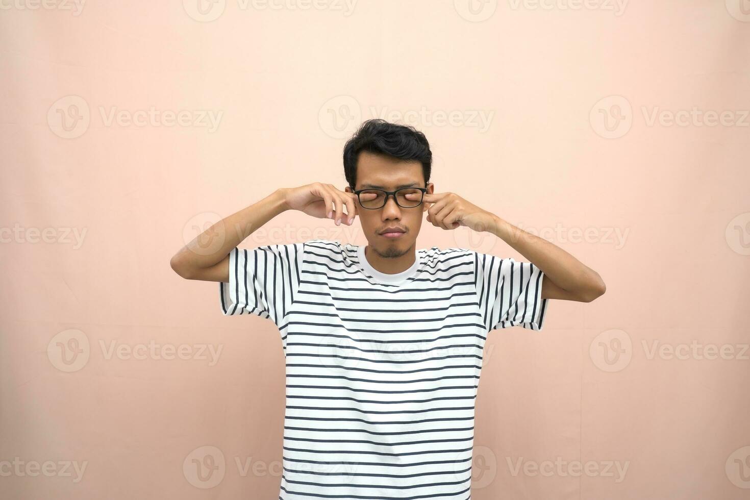 Porträt von ein asiatisch Mann tragen Brille tragen ein beiläufig gestreift T-Shirt. schläfrig Ausdruck während halten ein Titel gefüllt mit Schokolade Milch. isoliert Beige Hintergrund. foto
