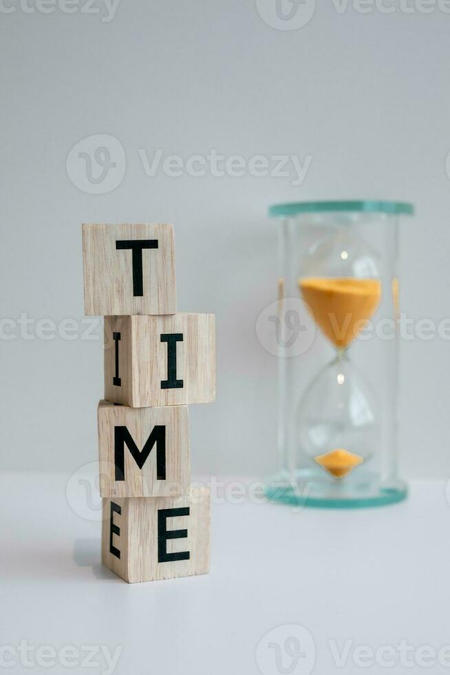 hölzern Blöcke mit das Wort Zeit geschrieben auf Es, gegen das Hintergrund von ein Sanduhr und Weiß Hintergrund. foto