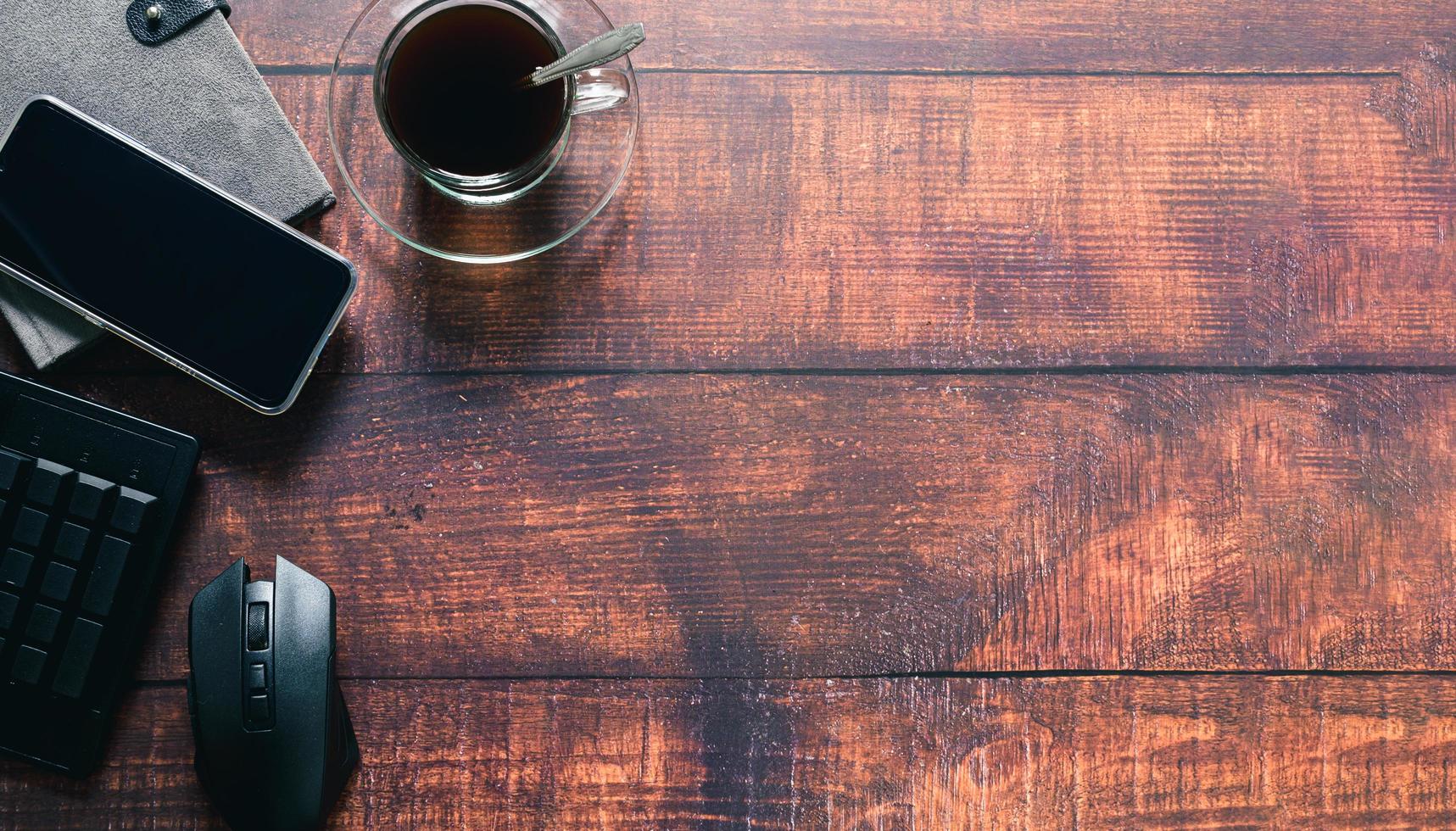 Kaffeetasse, Smartphone, Notebook, Tastatur, Maus stehen am Schreibtisch foto