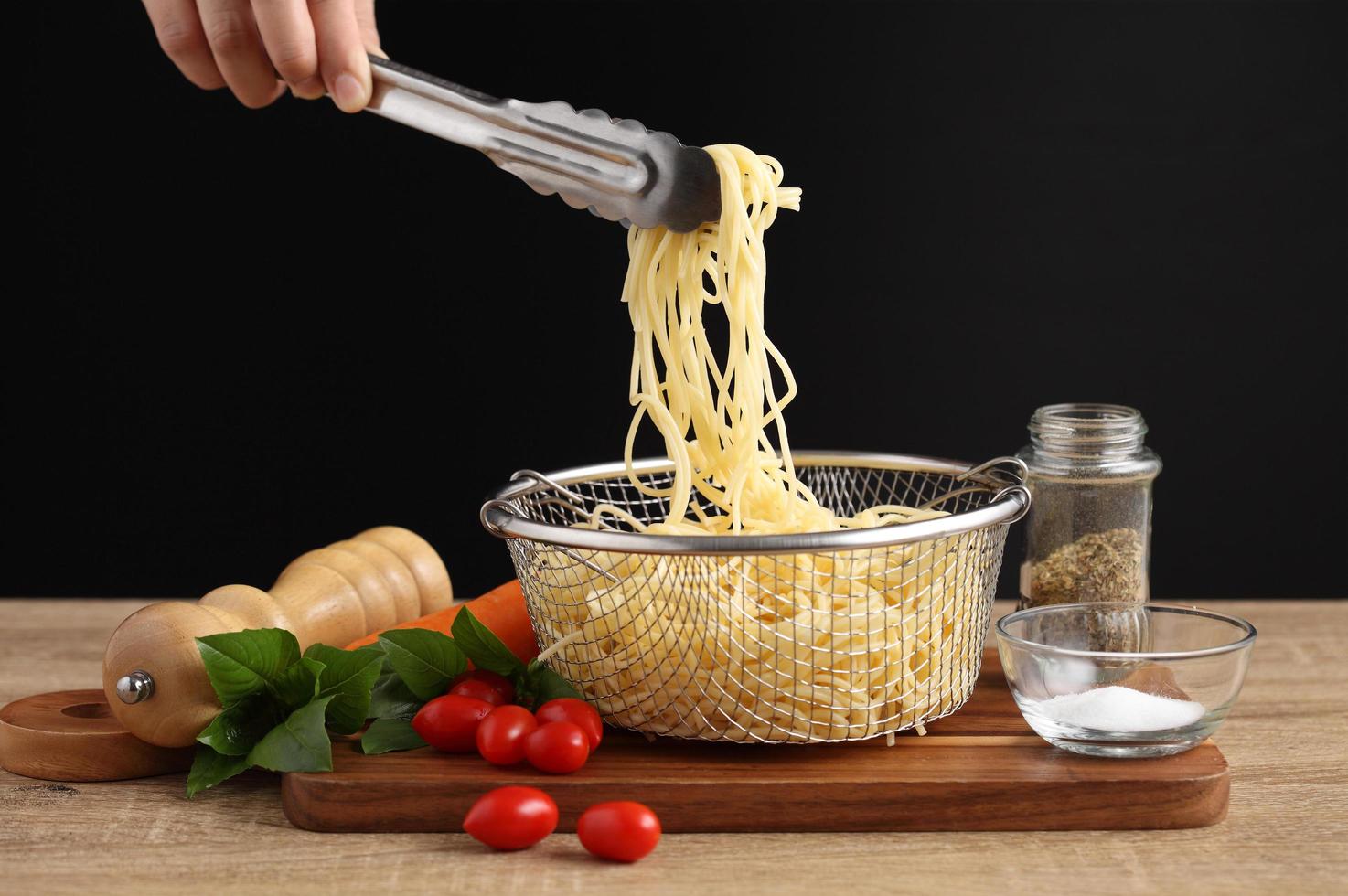 Hand hält Zange und gekochte Spaghetti aus Metallsieb foto