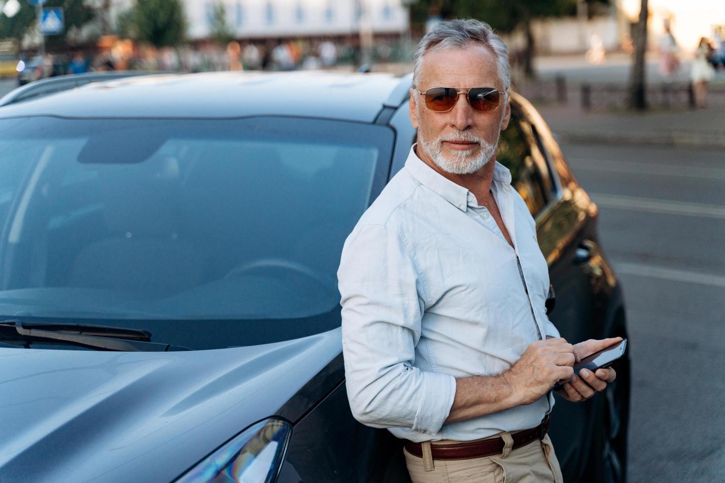 älterer Mann, der in der Nähe seines SUV-Autos steht und Smartphone hält. foto