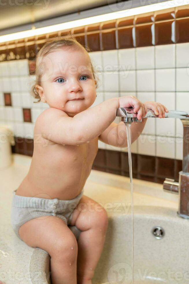 Lachen wenig Mädchen nimmt Hygiene Verfahren im das Waschbecken im das Küche foto