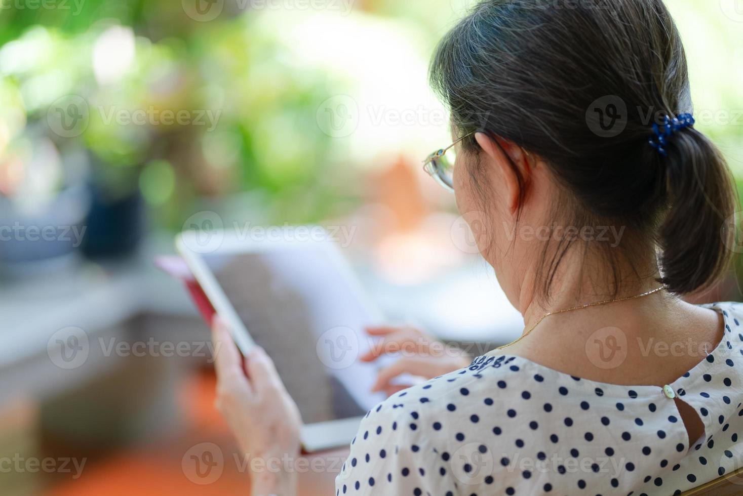 Senior asiatische Frau mit Tablet, um Social Media im Hausgarten zu spielen foto