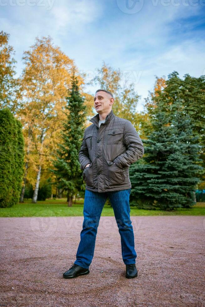 ein Mann im ein Herbst Jacke im das Park steht auf das Pfad foto