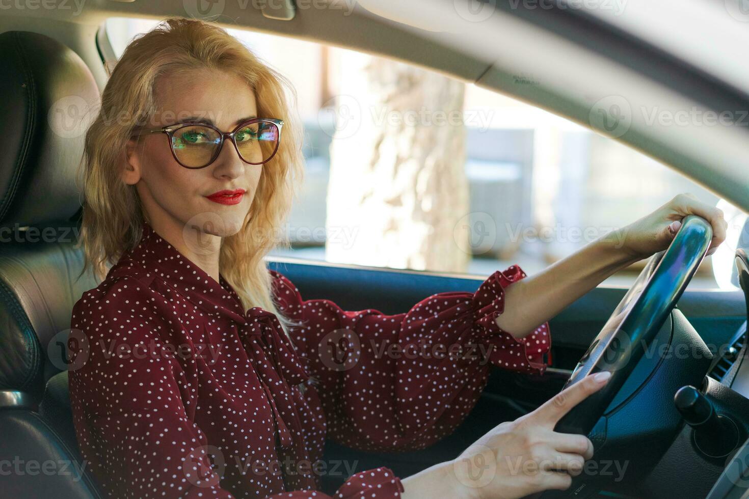 schön erfolgreich blond Frau im ein rot Kleid Sitzung im ein Auto hinter das Rad foto