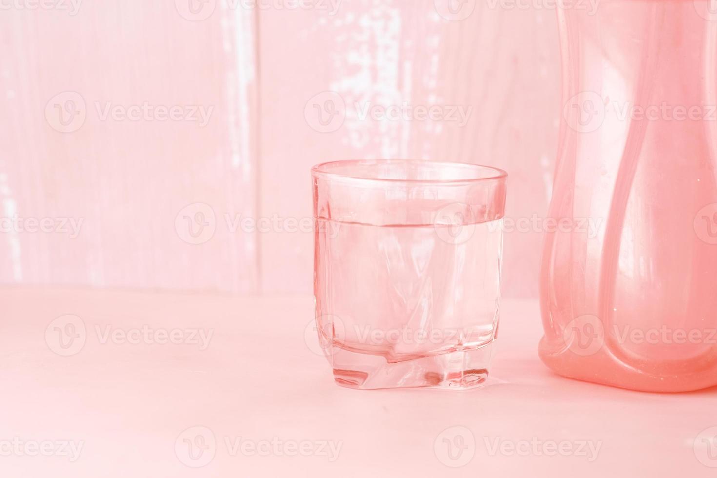 Glas Wasser und Plastikbehälter auf Rosa foto