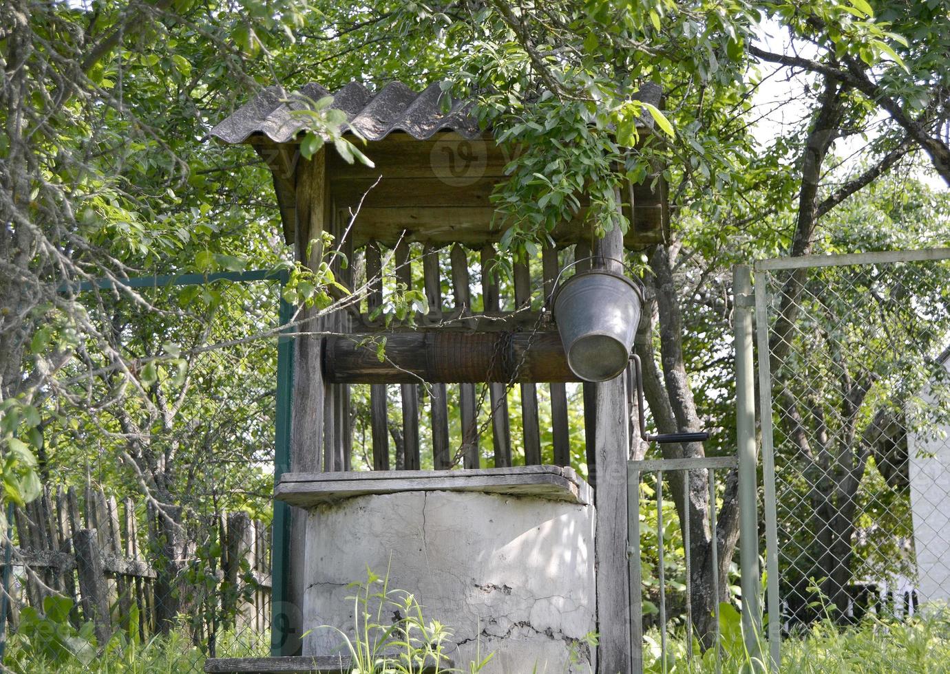 Brunnen mit Eiseneimer an langer Schmiedekette für sauberes Trinkwasser foto