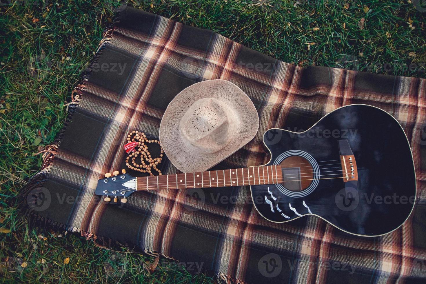 Gitarre und ein Strohhut liegen auf einem karierten Hintergrund auf grünem Gras foto