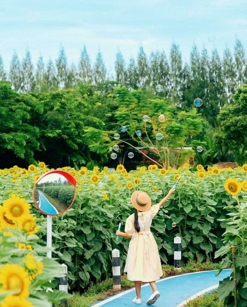 Pflege Natur ein blühen Reise von Wachstum und Schönheit Frau Stehen unter Blühen Blumen im Garten, umgeben durch üppig Laub und Baum. foto